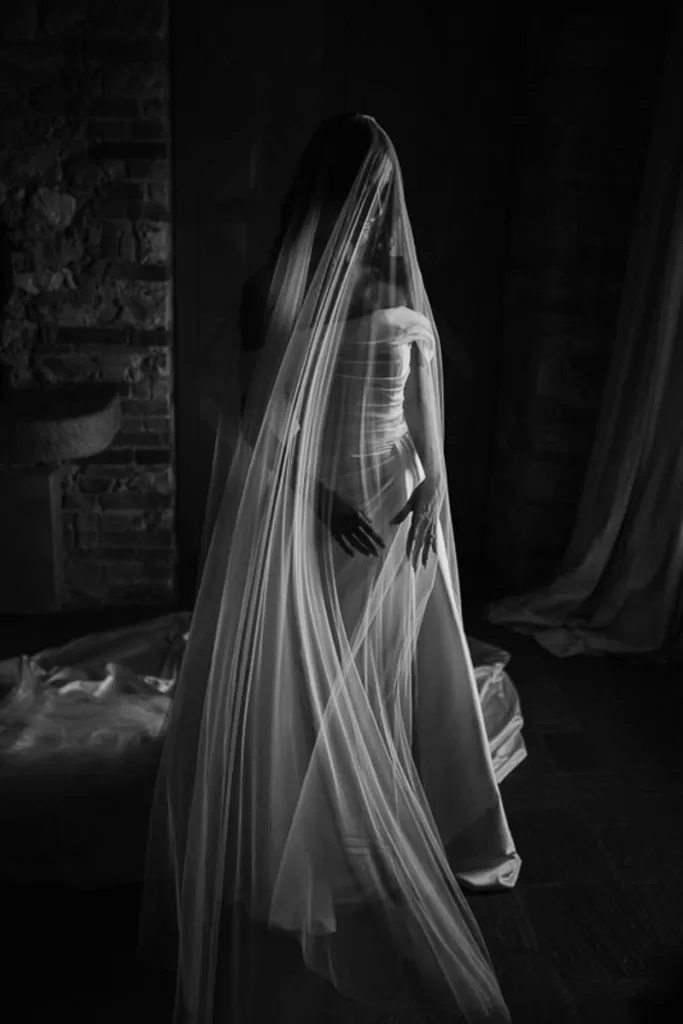A bride with a long veil covering her face looks down to the ground.