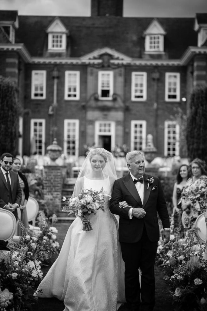 A bride and her father walk arm in arm down the aisle, taken by London Wedding Photographer Philip White.