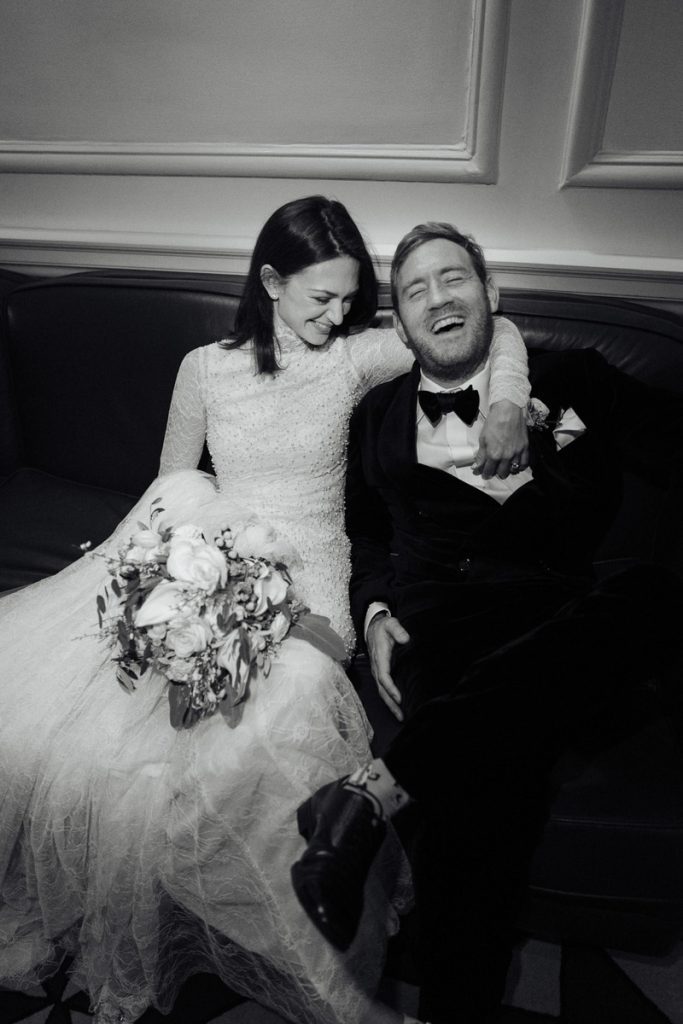 A newly married couple laugh together on a sofa captured by London wedding photographer Philip white.